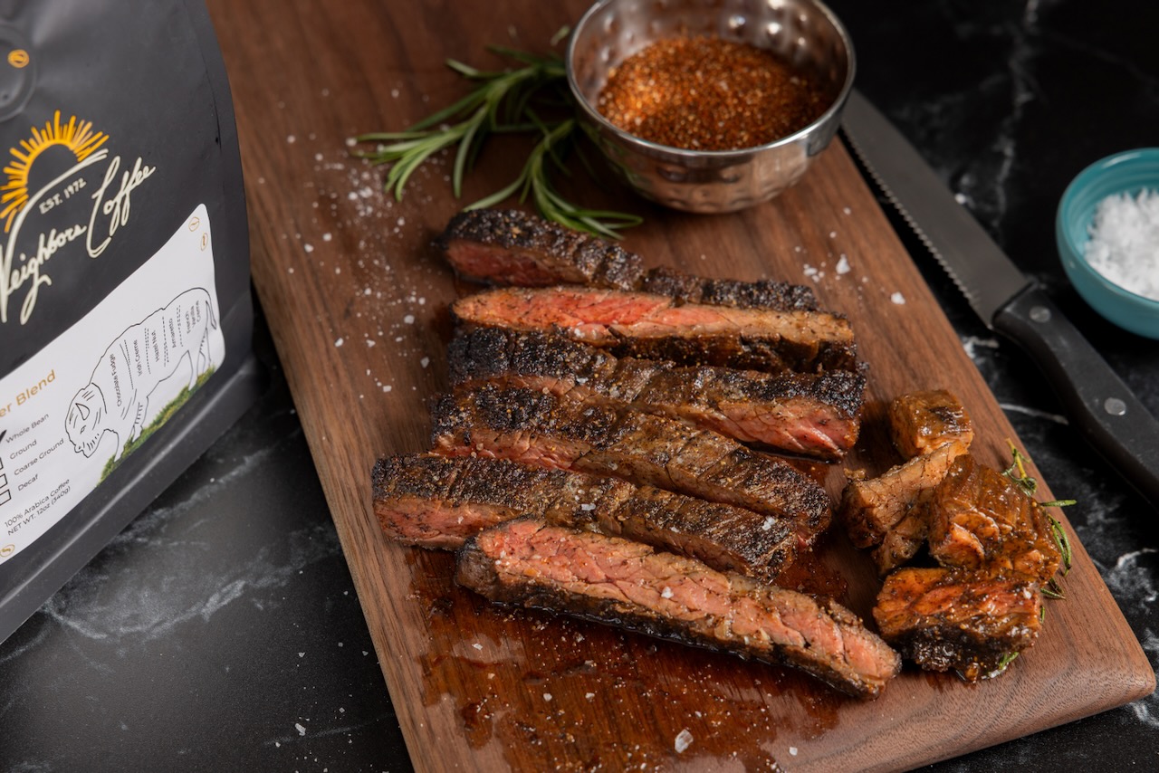Slices of medium-rare skirt steak rest on a wooden cutting board alongside a bag of coffee beans from Neighbors Coffee, based in Oklahoma City.